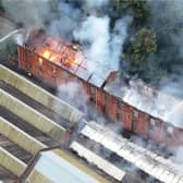 Flames and smoke pour from roof of factory building.
