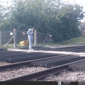 Teen stares at phone while stood on level crossing. Network Rail 