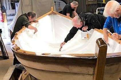 Rotarians are pictured applying the final coating of undercoat to the skiff’s interior. The top coats will be applied this week.