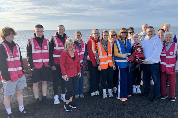 Arbroath Specsavers retail manager Jamie Buchan (white hoodie) presents run director Karen Archer i(blue high-vis) with the renewed portable defibrillator (pic: West Links parkrun)
